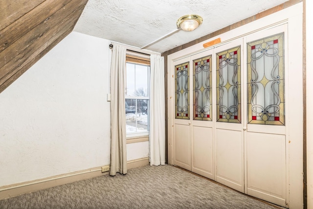 doorway to outside featuring carpet, a textured ceiling, and baseboards