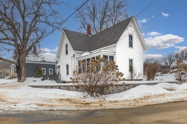 view of front facade with roof with shingles and a chimney