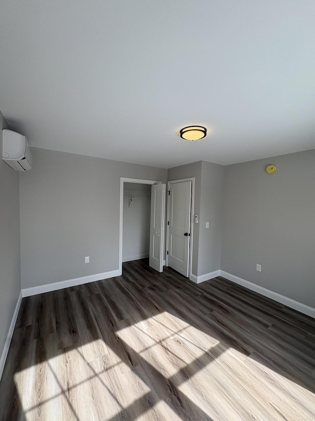 unfurnished room with a wall mounted AC, dark wood finished floors, and baseboards