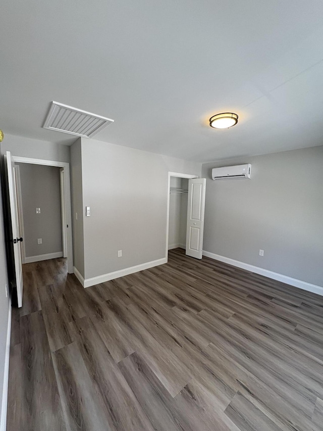 unfurnished bedroom featuring an AC wall unit, wood finished floors, visible vents, and baseboards