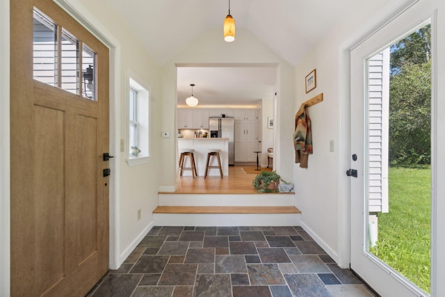 foyer entrance with a wealth of natural light, lofted ceiling, stone finish floor, and baseboards