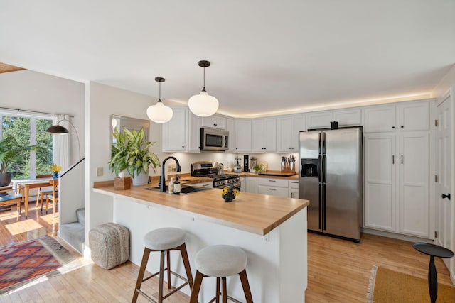 kitchen featuring light wood-style flooring, a breakfast bar, a peninsula, stainless steel appliances, and a sink