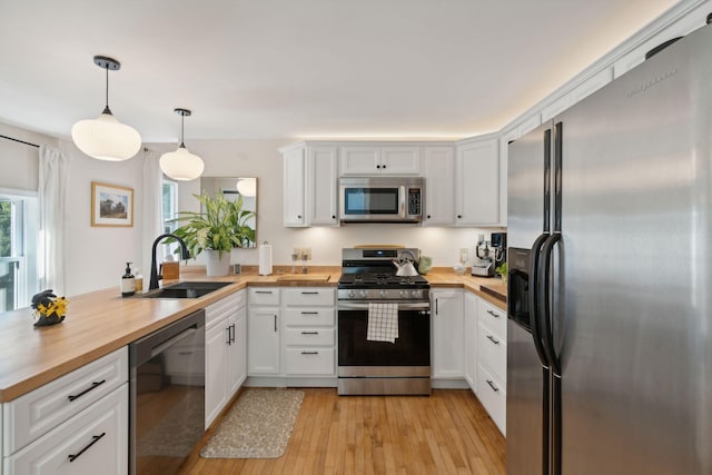 kitchen featuring stainless steel appliances, a sink, wood counters, and a peninsula