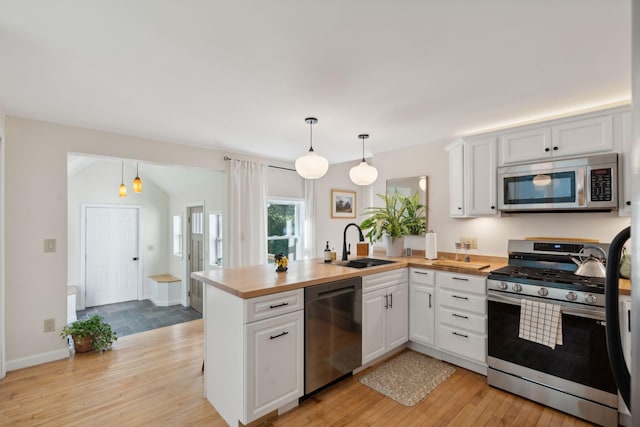 kitchen featuring butcher block counters, appliances with stainless steel finishes, light wood-style floors, a sink, and a peninsula