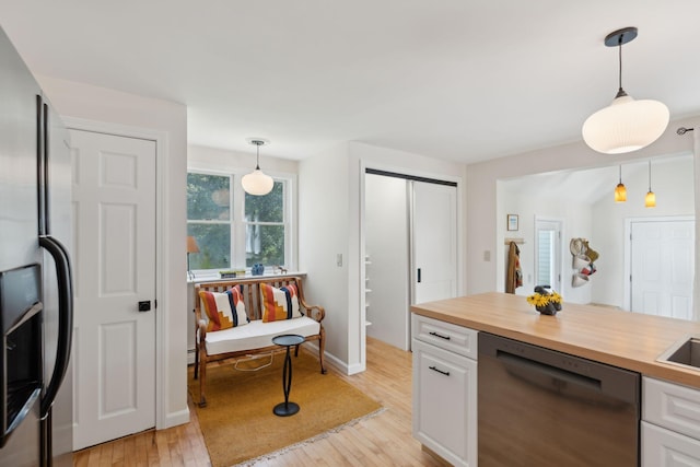 kitchen with stainless steel appliances, butcher block counters, white cabinets, light wood finished floors, and decorative light fixtures