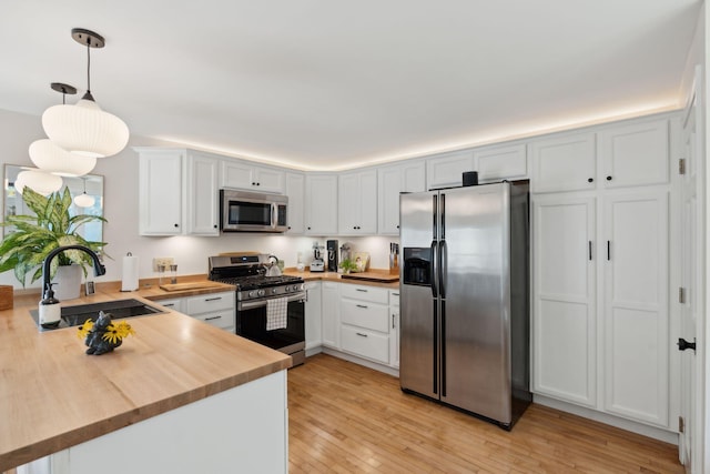 kitchen with stainless steel appliances, a peninsula, a sink, light wood finished floors, and pendant lighting