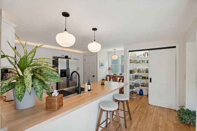 kitchen with light wood finished floors, stainless steel fridge with ice dispenser, a breakfast bar, hanging light fixtures, and a sink