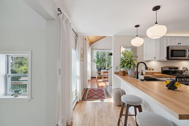 kitchen with stainless steel appliances, a breakfast bar, a sink, light wood-style floors, and decorative light fixtures