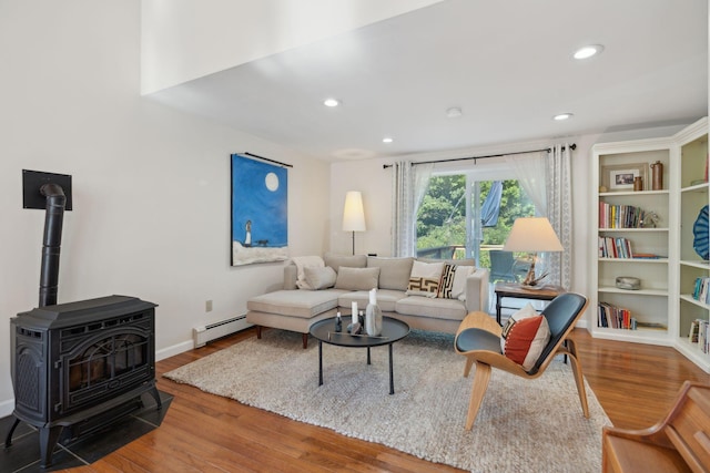 living area featuring a baseboard heating unit, wood finished floors, a wood stove, and recessed lighting