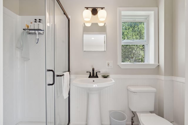 bathroom with a stall shower, wainscoting, a sink, and toilet