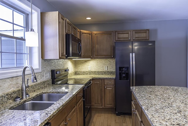 kitchen featuring decorative backsplash, a sink, black appliances, and light stone countertops