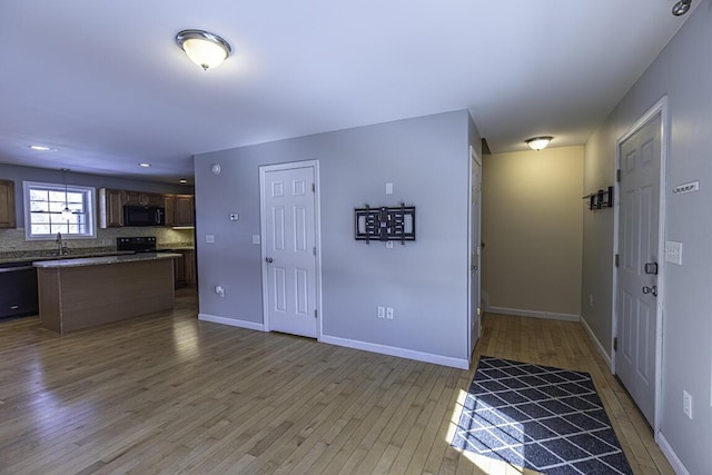 kitchen featuring baseboards, a center island, light wood-type flooring, black appliances, and backsplash