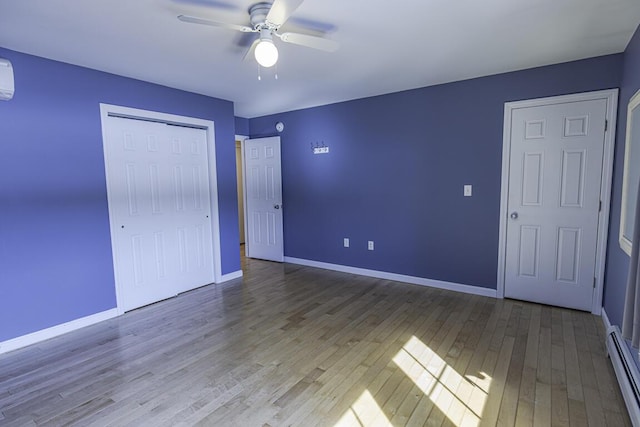 unfurnished bedroom with a closet, a baseboard heating unit, a ceiling fan, wood finished floors, and baseboards