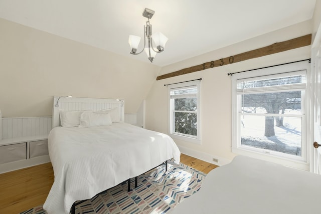 bedroom with lofted ceiling, wainscoting, wood finished floors, and a notable chandelier