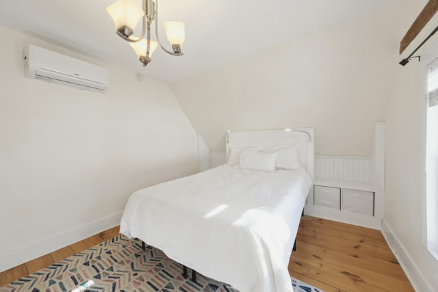 bedroom with a chandelier, a wall mounted AC, wood finished floors, and baseboards