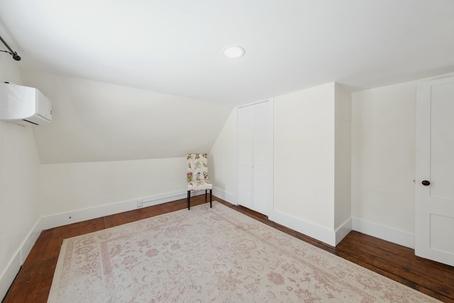 additional living space with dark wood-type flooring, a wall unit AC, vaulted ceiling, and baseboards