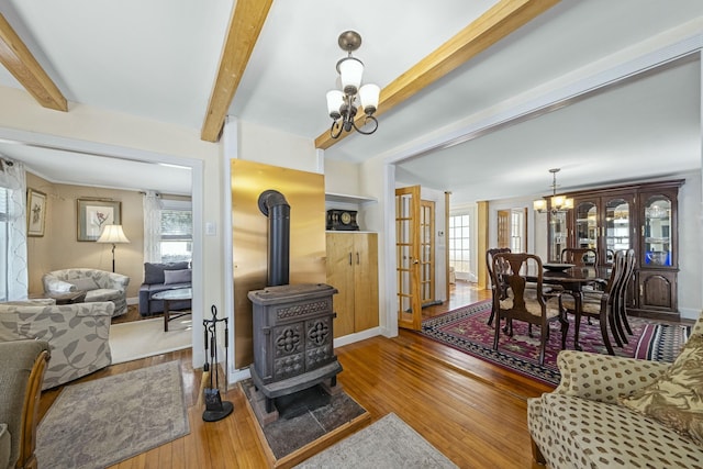 living room featuring beam ceiling, a healthy amount of sunlight, a wood stove, and an inviting chandelier