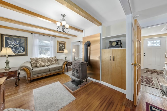 living room featuring light wood-style floors, a wood stove, a chandelier, and beam ceiling