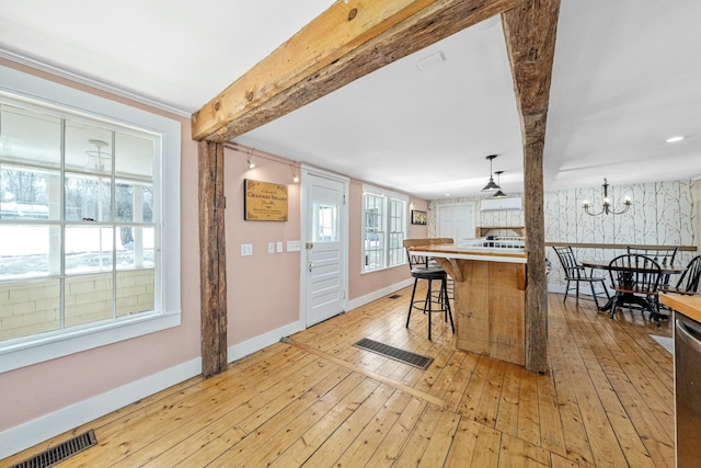 kitchen featuring visible vents, a breakfast bar, light countertops, pendant lighting, and beam ceiling