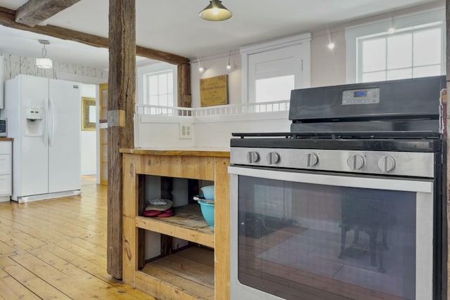 kitchen with white refrigerator with ice dispenser, beam ceiling, light wood finished floors, light countertops, and stainless steel range with gas stovetop