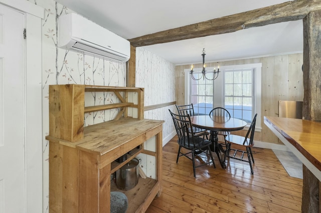 dining area featuring a chandelier, wood finished floors, baseboards, a wall mounted AC, and beam ceiling