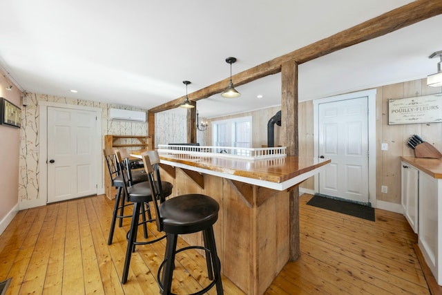 kitchen featuring a peninsula, light countertops, a wall mounted AC, light wood finished floors, and decorative light fixtures