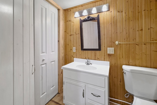 half bathroom featuring wooden walls, a closet, vanity, and toilet