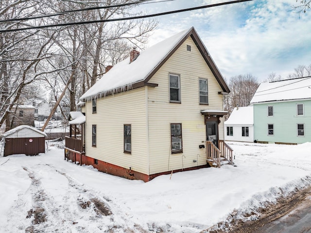 snow covered property with an outbuilding, a chimney, and a shed