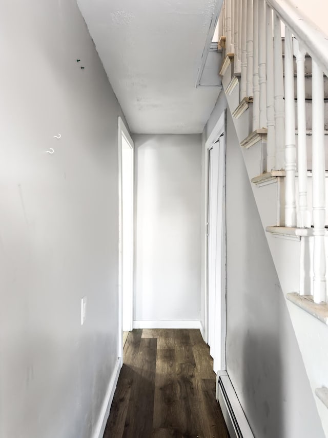 corridor featuring dark wood-style floors, a baseboard radiator, baseboards, and stairs