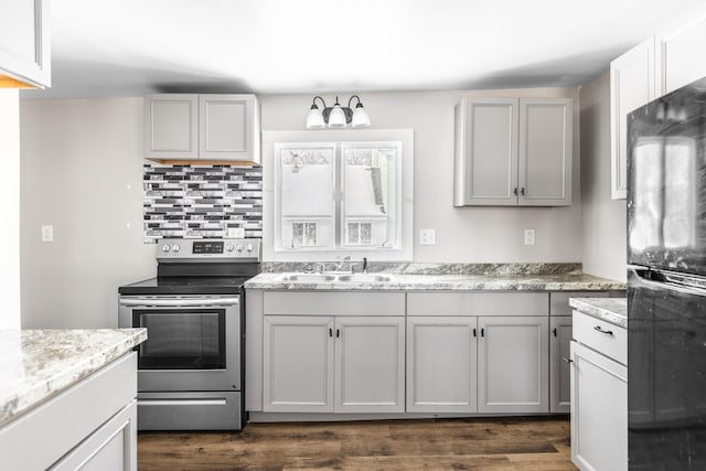 kitchen featuring black refrigerator, a sink, stainless steel range with electric cooktop, decorative backsplash, and dark wood finished floors