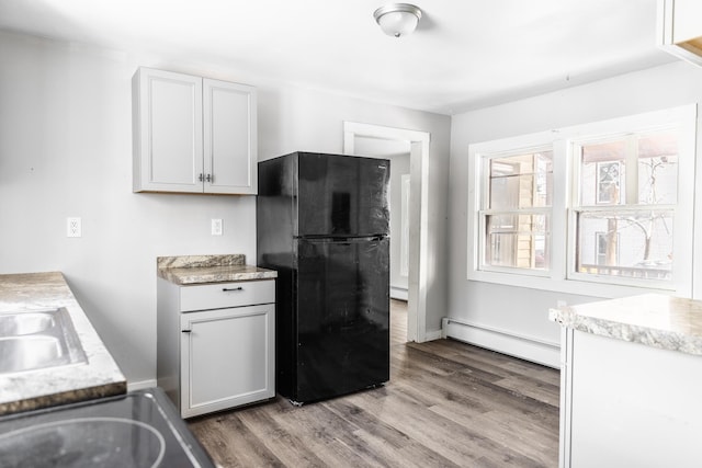 kitchen with wood finished floors, freestanding refrigerator, baseboard heating, light countertops, and a sink