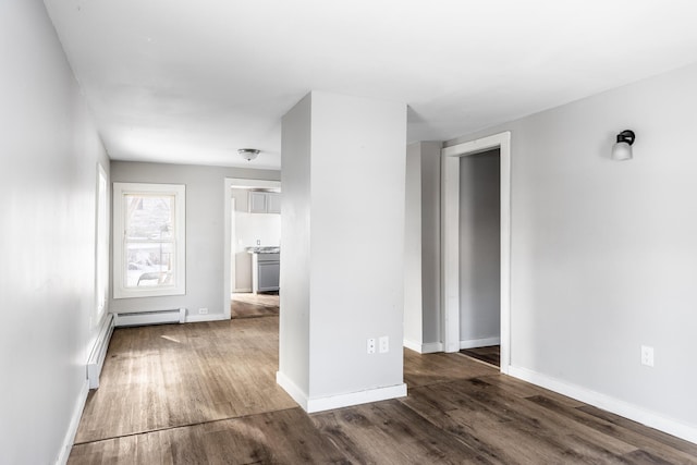 empty room featuring a baseboard heating unit, baseboards, and dark wood finished floors