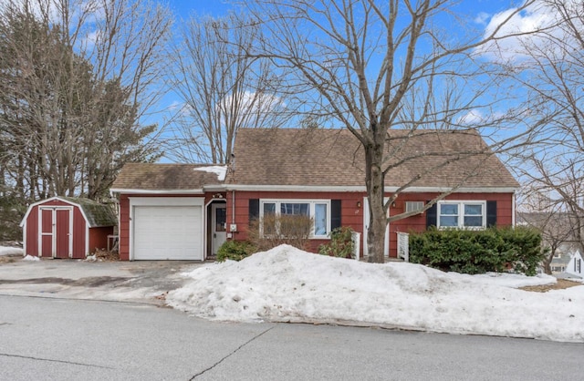 cape cod house featuring a garage, driveway, an outbuilding, roof with shingles, and a storage unit