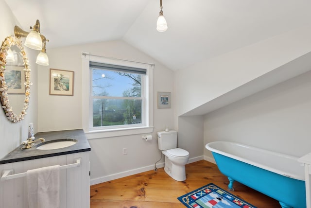 full bath with wood finished floors, lofted ceiling, toilet, vanity, and a freestanding tub