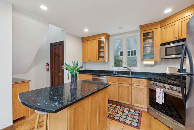 kitchen with appliances with stainless steel finishes, a sink, light wood-type flooring, a center island, and dark stone countertops