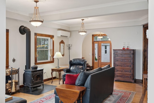 living room featuring an AC wall unit, light wood-style flooring, a wood stove, arched walkways, and baseboards