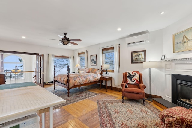 bedroom featuring an AC wall unit, a glass covered fireplace, multiple windows, light wood-style floors, and recessed lighting