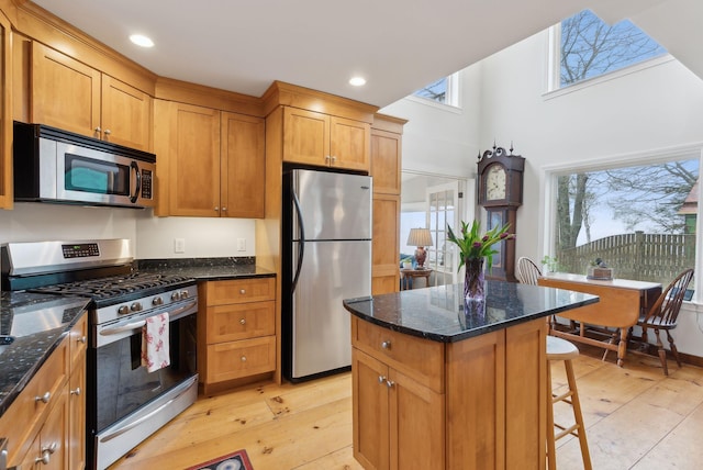 kitchen with stainless steel appliances, dark stone counters, a center island, light wood-style floors, and a kitchen bar