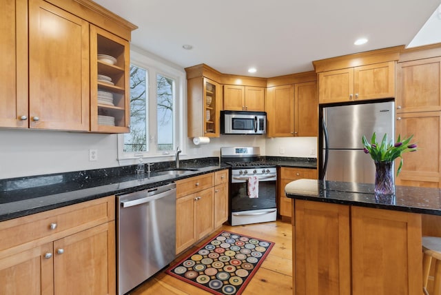 kitchen featuring appliances with stainless steel finishes, a sink, glass insert cabinets, dark stone countertops, and recessed lighting