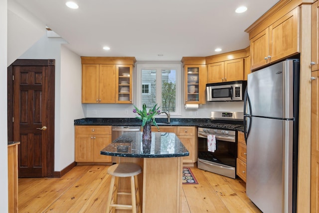 kitchen featuring appliances with stainless steel finishes, light wood-style floors, a kitchen island, dark stone countertops, and glass insert cabinets
