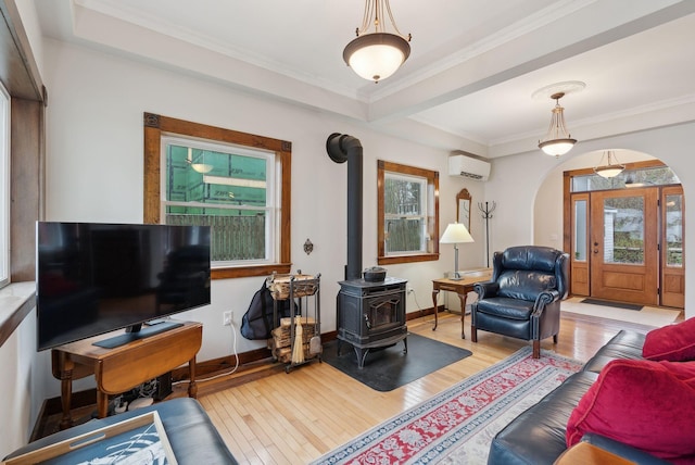 living room with an AC wall unit, a wood stove, arched walkways, wood finished floors, and crown molding