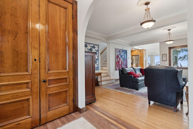 hall with light wood-style floors, ornamental molding, stairs, arched walkways, and baseboards