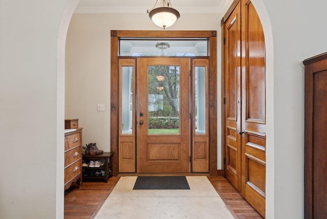 foyer with arched walkways, light wood finished floors, and crown molding