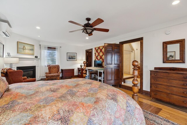 bedroom featuring a wall mounted AC, wood finished floors, a glass covered fireplace, recessed lighting, and a ceiling fan