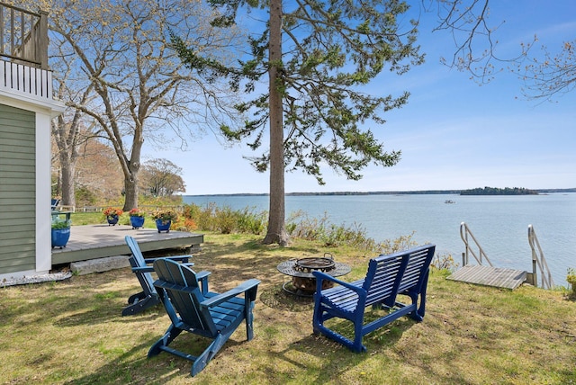 view of grassy yard featuring an outdoor fire pit and a deck with water view