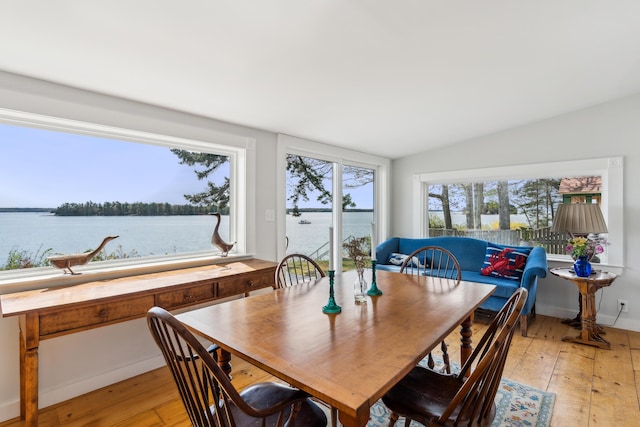 dining space with light wood-style flooring, lofted ceiling, and a water view
