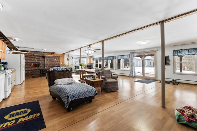 living room featuring light wood-style floors, a wood stove, baseboard heating, and a ceiling fan