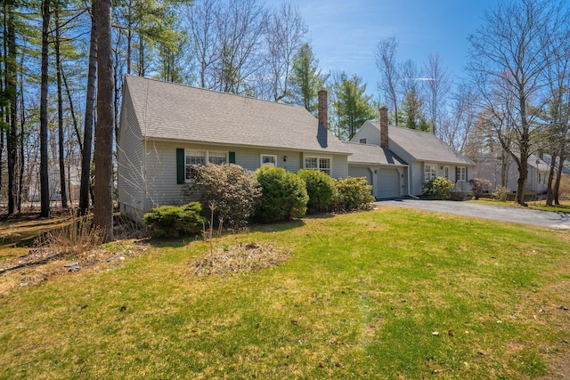 view of front of house with aphalt driveway, a chimney, roof with shingles, a front lawn, and an attached garage