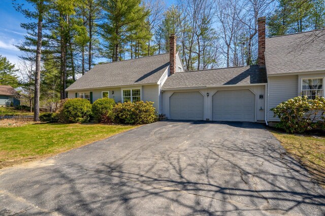 view of front of property with an attached garage, a chimney, a front lawn, and aphalt driveway