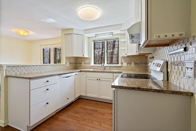 kitchen with a sink, white appliances, hardwood / wood-style floors, a peninsula, and backsplash